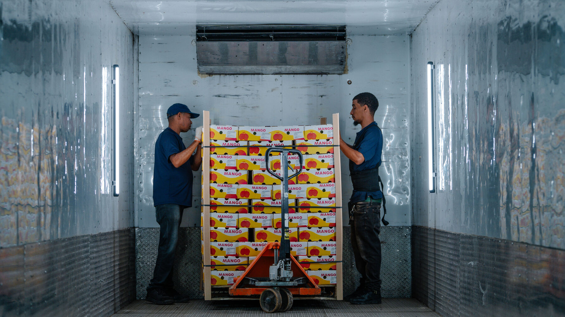 Dos operarios introducen un pallet de cajas de fruta en un contenedor refrigerado.